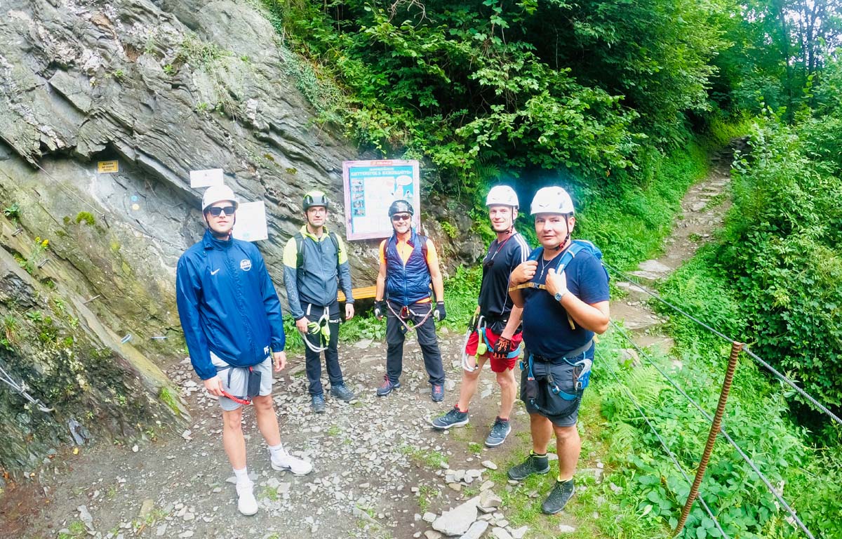 Gruppe mit Kletterausrüstung steht am Beginn eines Wanderwegs