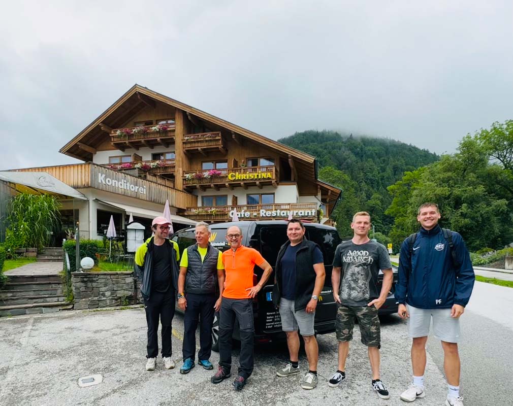 Gruppe steht vor einem Gasthaus mit Autos im Hintergrund