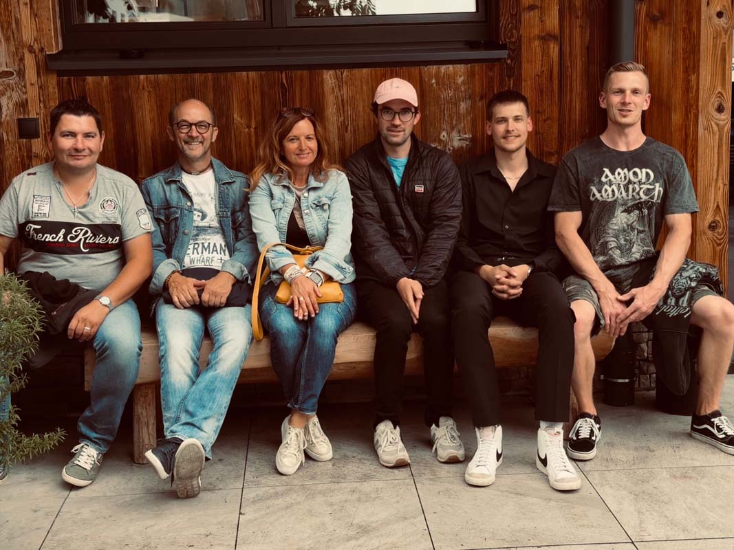 Fünf Personen sitzen auf einer Holzbank und lächeln in die Kamera