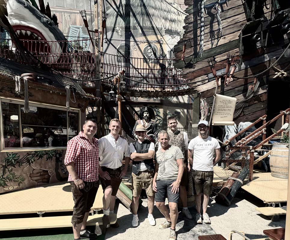 Mehrere Männer stehen in einem Freizeitpark vor einer Piratenschiff-Kulisse