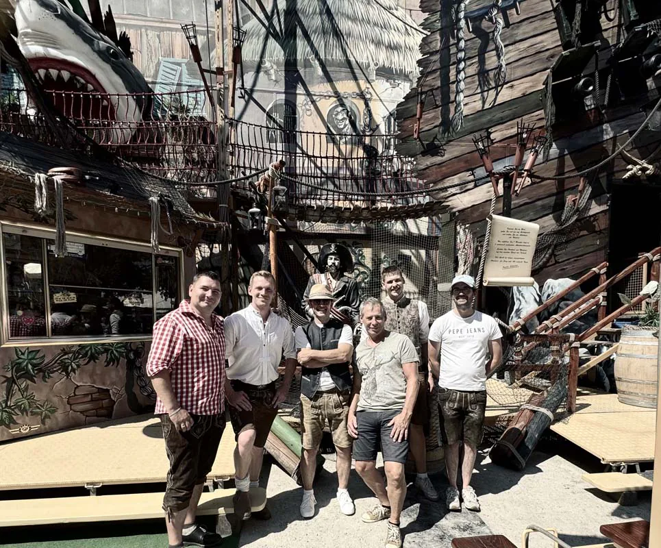 Mehrere Männer stehen in einem Freizeitpark vor einer Piratenschiff-Kulisse