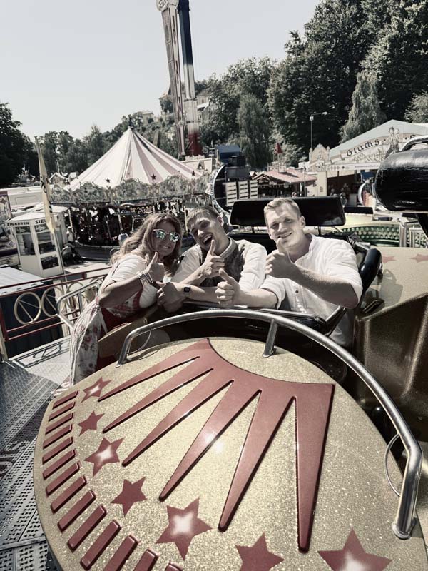 Drei Personen sitzen in einem Fahrgeschäft und posieren für die Kamera