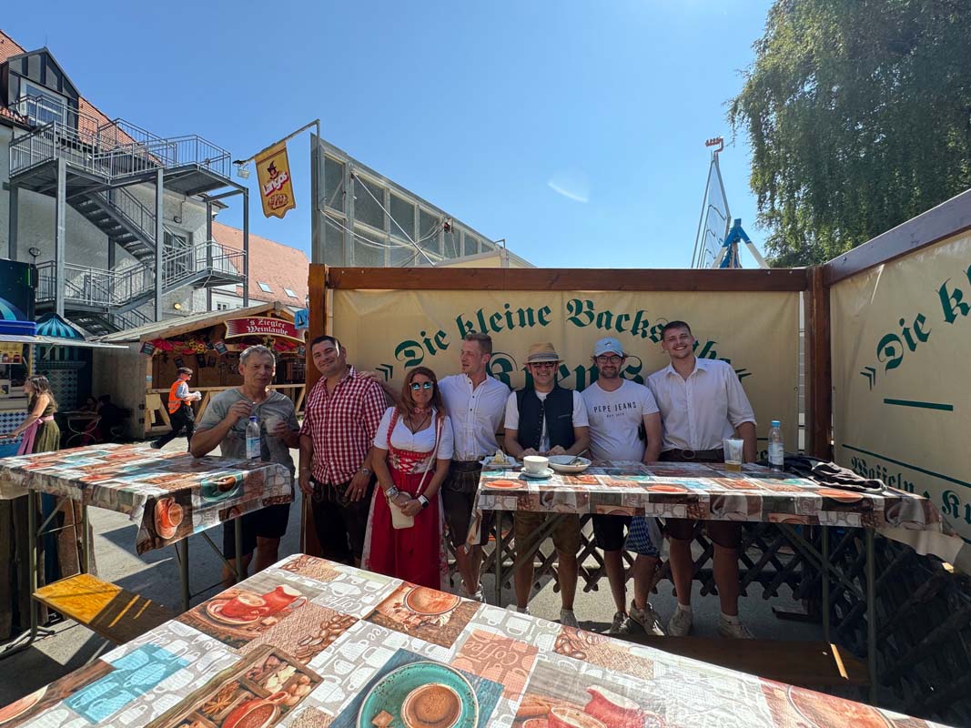 Gruppe steht an einem Stand mit Tischen auf einem Volksfest