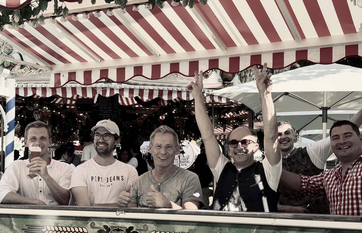 Gruppe von Männern feiert gemeinsam unter rot-weiß gestreiftem Zeltdach