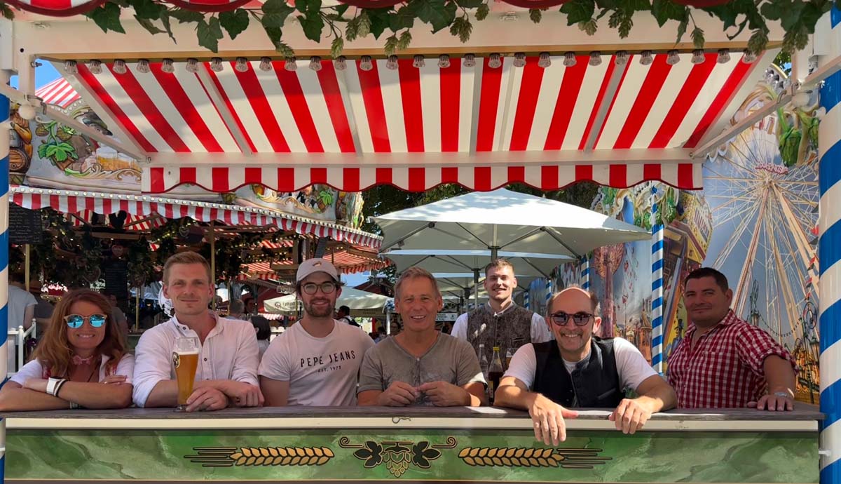 Männer sitzen lachend an einem Biertisch unter Markise