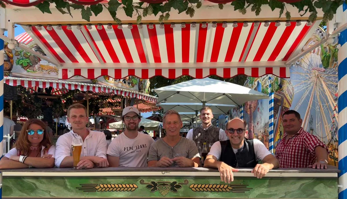 Männer sitzen lachend an einem Biertisch unter Markise