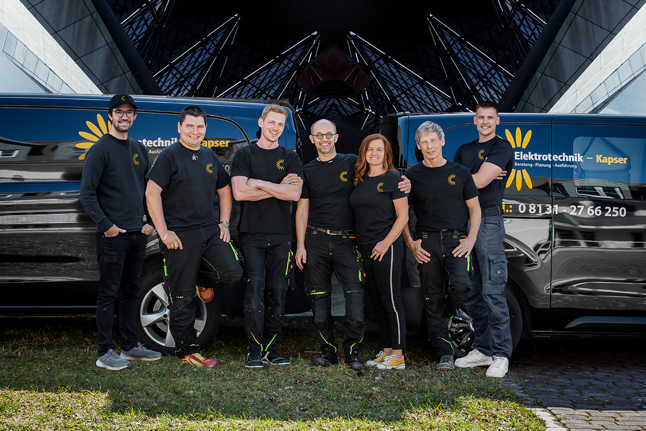 Teamfoto mit zwei Firmenfahrzeugen im Hintergrund