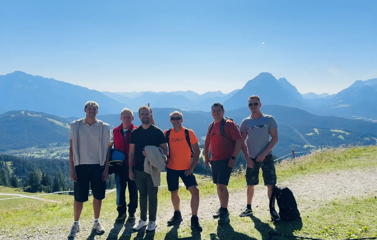 Sechs Kollegen posieren für ein Gruppenfoto vor Bergpanorama