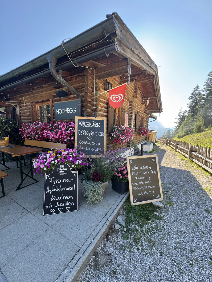 Almhütte mit Blumenschmuck und Tafeln am Eingang in der Abendsonne