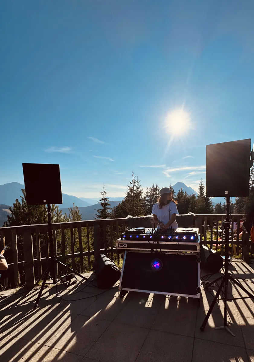 DJ spielt auf der Almterrasse vor Bergkulisse in der Abendsonne