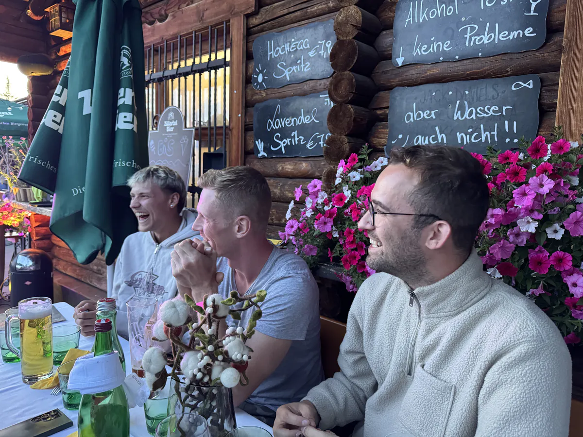 Drei Kollegen lachen an der Tafel vor der Hüttenwand