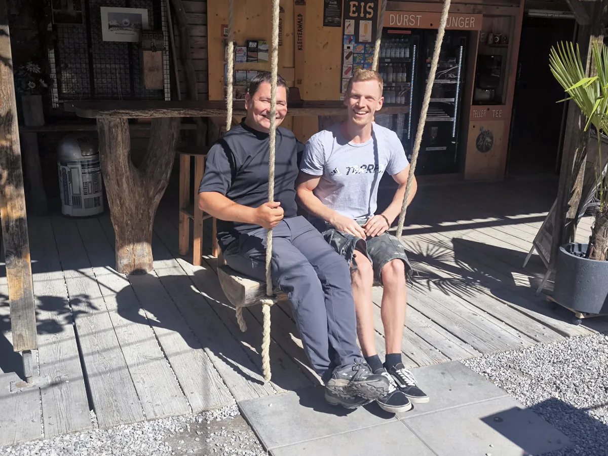 Zwei Kollegen sitzen in der Sonne auf einer Bank vor der Hütte