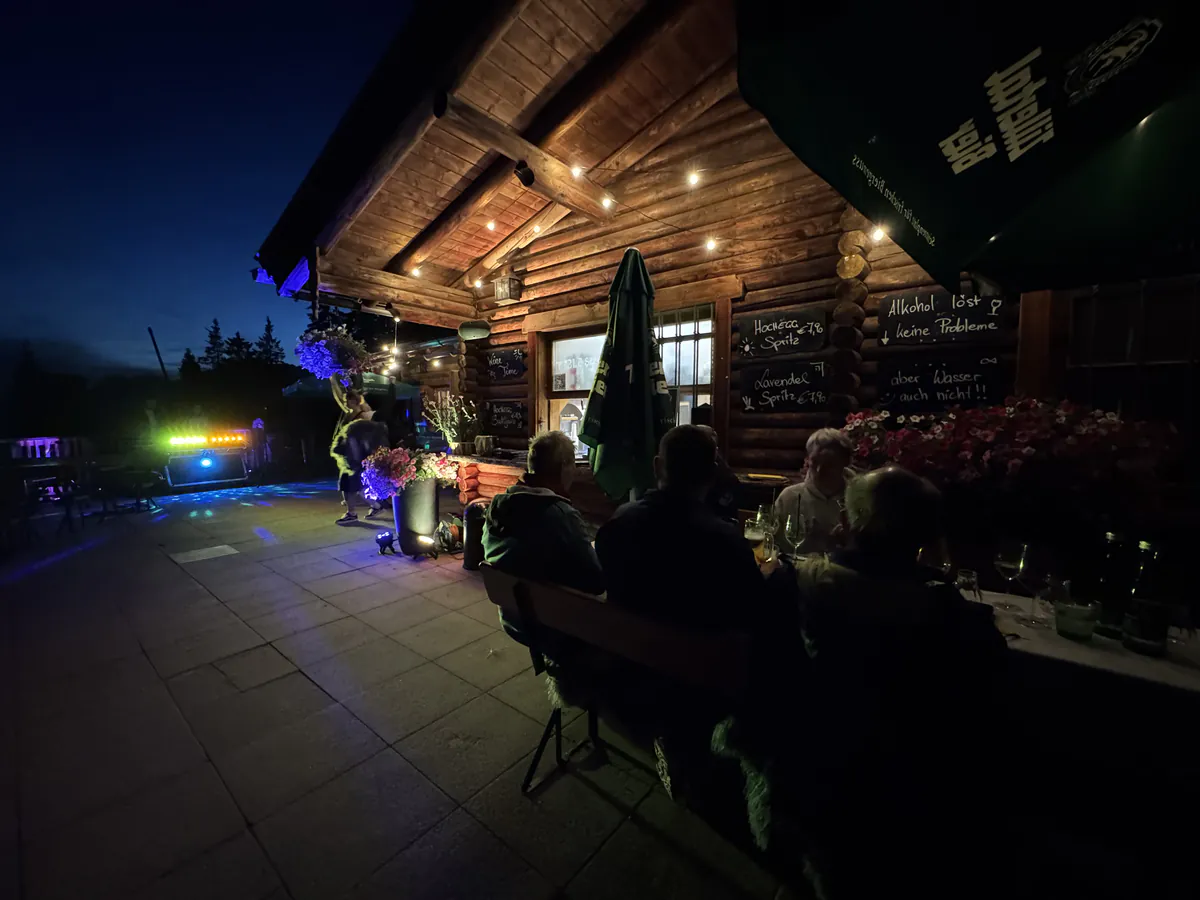 Beleuchtete Almhütte am Abend mit Gästen auf der Terrasse