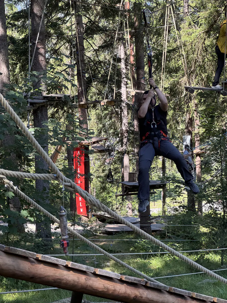 Kollege klettert gesichert an einem Seilelement zwischen hohen Bäumen