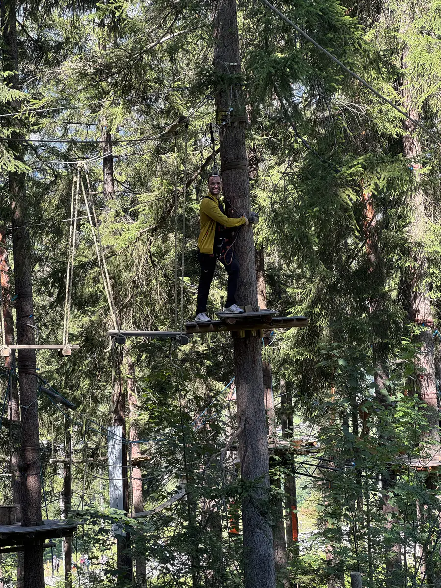 Person balanciert über einen Holzsteg hoch oben im Hochseilgarten