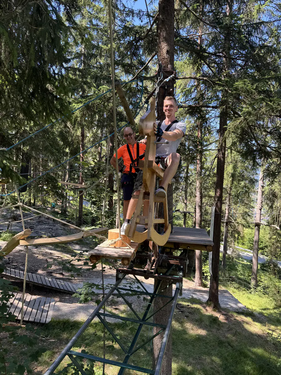 Zwei Kollegen sitzen gesichert auf einer Plattform im Kletterwald
