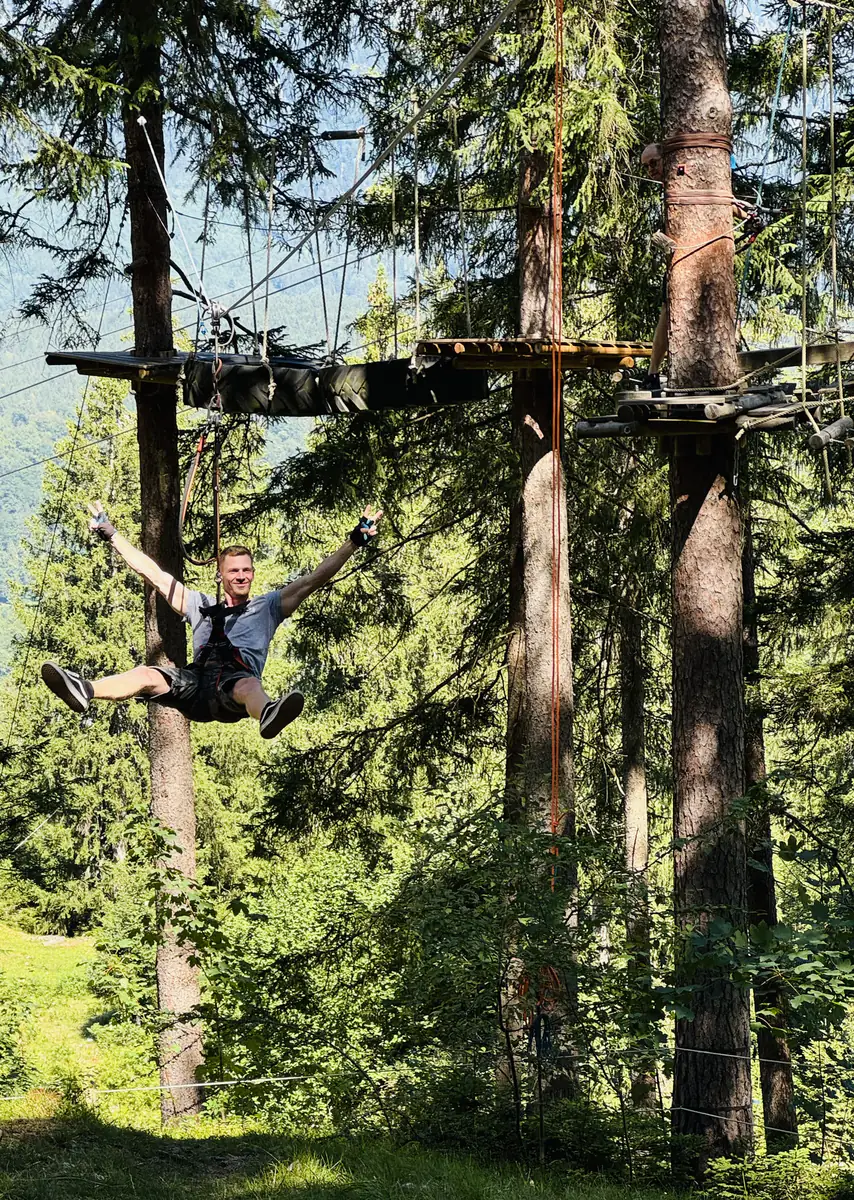 Kollege gleitet mit ausgebreiteten Armen an der Seilrutsche durch den Wald
