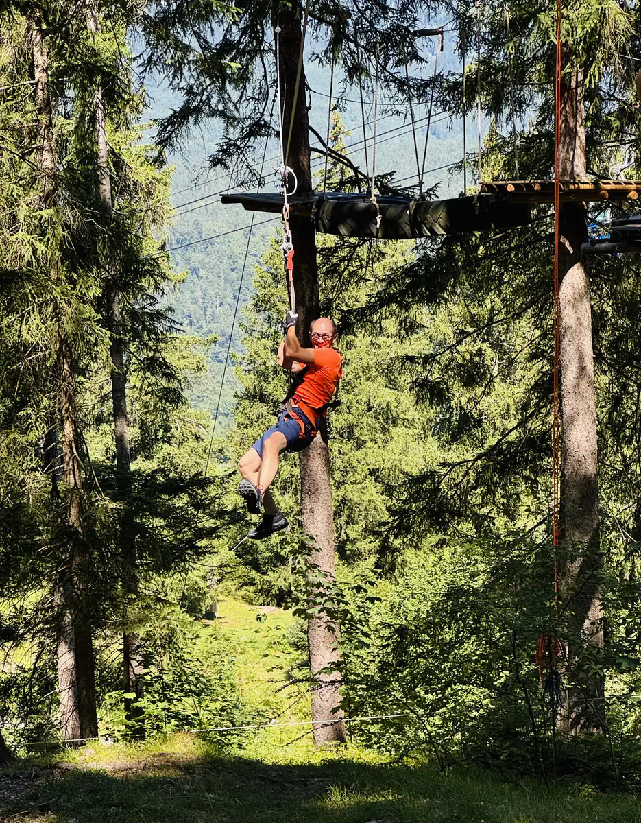 Kletterer im orangefarbenen Shirt hängt im Gurt an einer Seilbahn