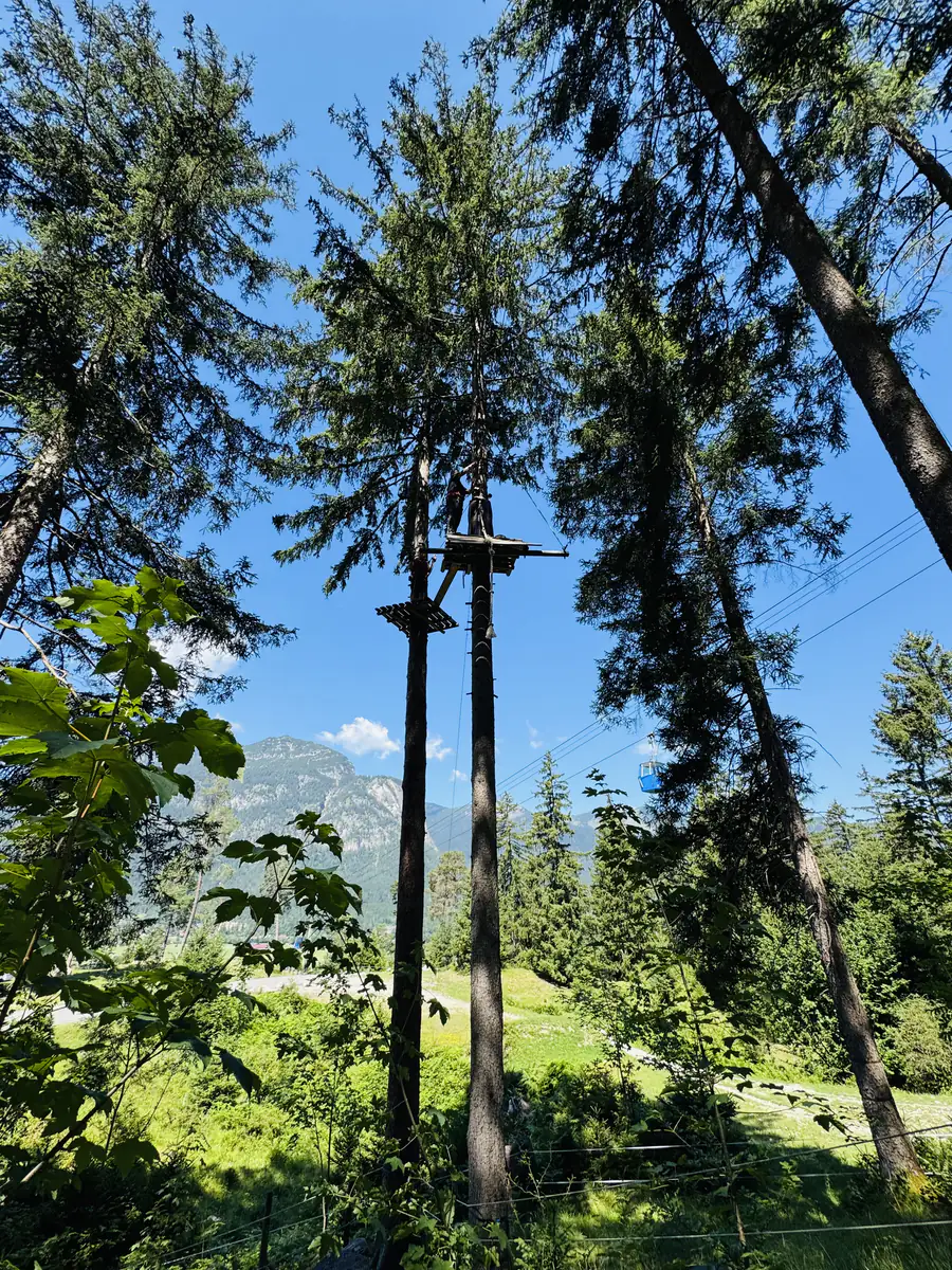 Kletterturm des Hochseilgartens vor blauem Himmel und Bergpanorama